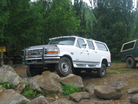 1995 Ford C-350 (Centurion Conversions) - White SUV with aftermarket grille guard parked on rocks, with another SUV in the background.