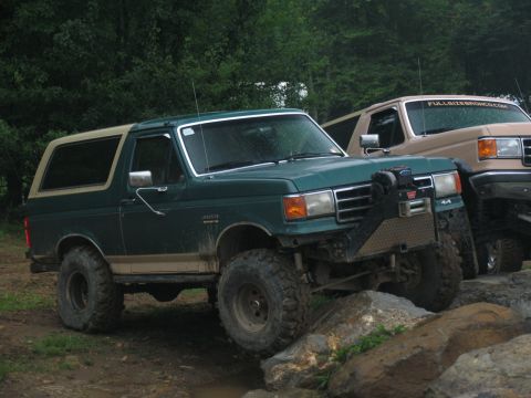 1995 Ford C-350 (Centurion Conversions) - A green Ford Bronco with a tan top navigates rocky terrain, with another Bronco visible behind it.