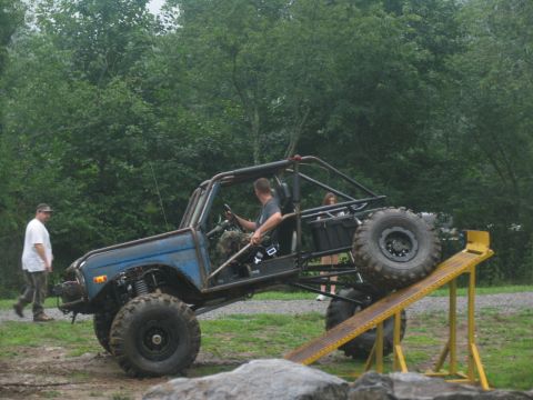 1995 Ford C-350 (Centurion Conversions) - Modified off-road vehicle with large tires navigates a yellow ramp in an outdoor setting.