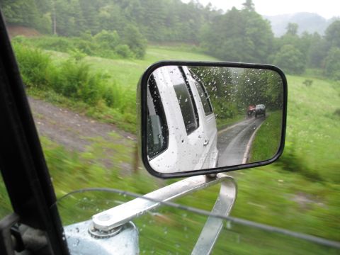 1995 Ford C-350 (Centurion Conversions) - Two trucks drive down a wet road on a cloudy day, seen from the side mirror.