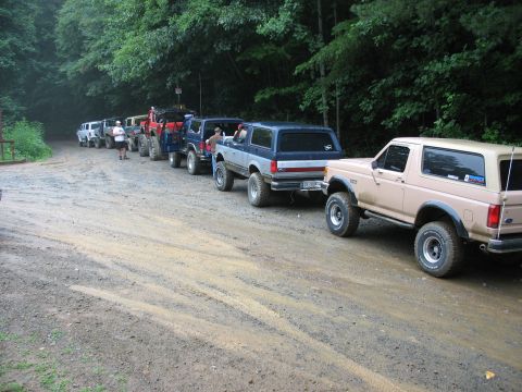 1995 Ford C-350 (Centurion Conversions) - Several Ford Broncos are lined up on a dirt road surrounded by trees.