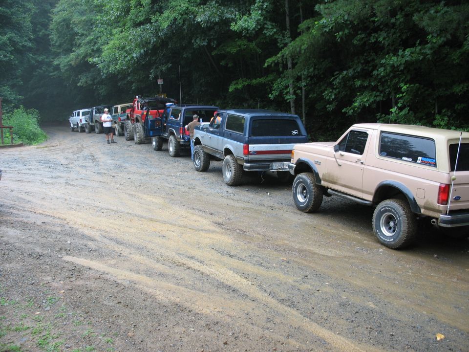Line of Ford Broncos on a dirt road, one tan Bronco in foreground