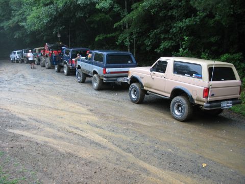 1995 Ford C-350 (Centurion Conversions) - A convoy of Ford Broncos parked on a muddy, tree-lined dirt road.