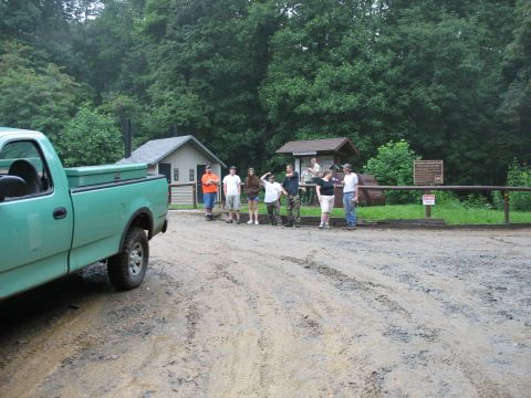 1995 Ford C-350 (Centurion Conversions) - A green pickup truck is parked on a muddy surface, with several people gathered near buildings in the background.