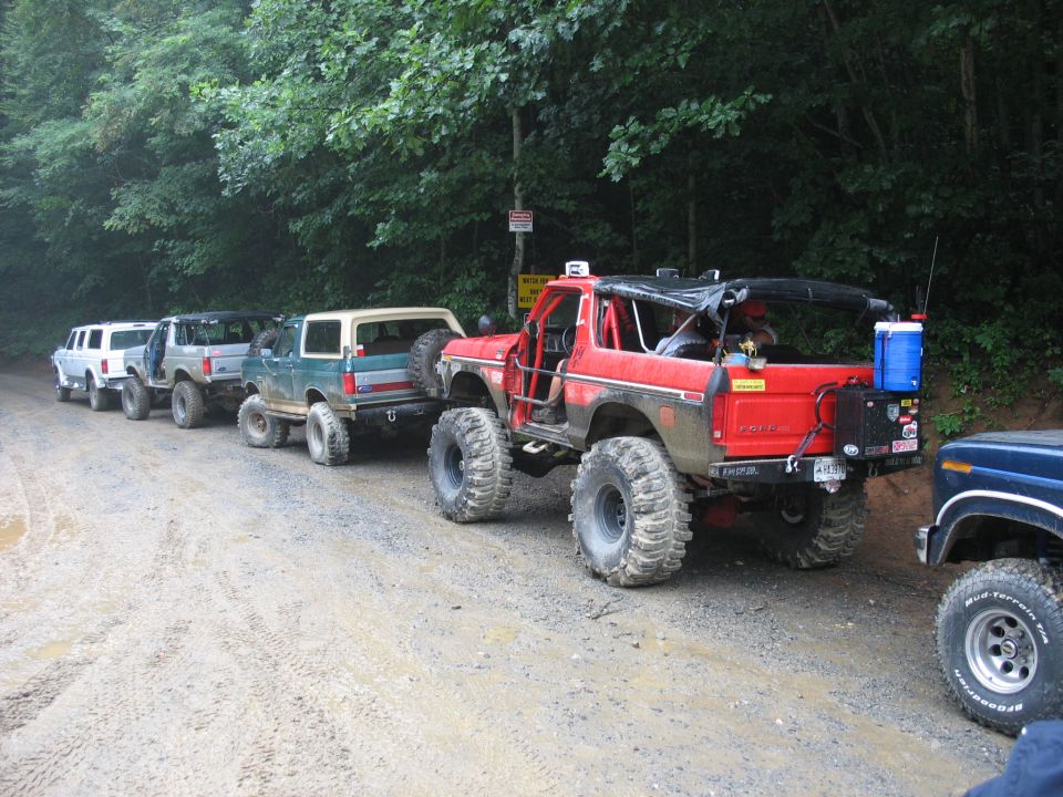 Red off-road Bronco with large tires and roll cage, parked on a dirt road