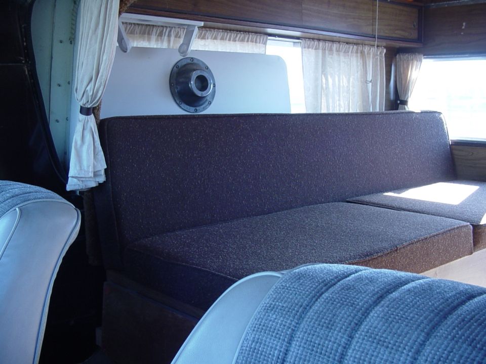 Interior of camper or RV showing fabric bench seat, side window with curtains and vents