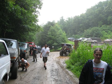 1995 Ford C-350 (Centurion Conversions) - A group of off-road enthusiasts and their trucks gather on a wet, muddy path surrounded by trees.