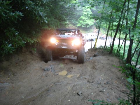 1995 Ford C-350 (Centurion Conversions) - A vehicle navigates a challenging muddy path surrounded by dense trees.