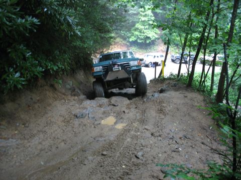 1995 Ford C-350 (Centurion Conversions) - An off-road truck with a winch navigates a challenging muddy and rocky trail, with other vehicles parked in the background.