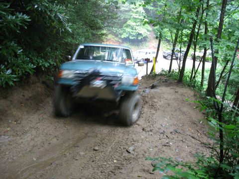1995 Ford C-350 (Centurion Conversions) - Off-road vehicle driving through mud on a wooded trail.