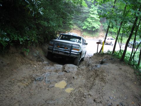 1995 Ford C-350 (Centurion Conversions) - A 1995 Ford C-350 (Centurion Conversions) tackles a challenging muddy and rocky off-road trail, with other vehicles visible in the backgrou…