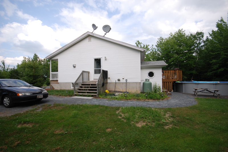 dark sedan parked on gravel driveway next to a white house with a deck and above-ground pool