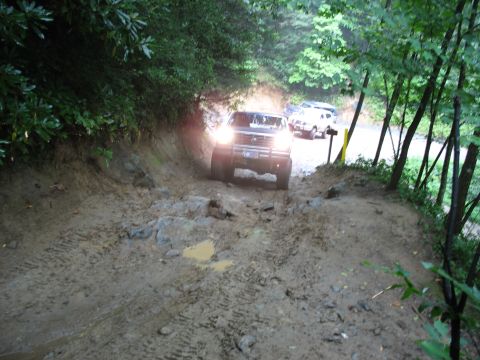 1995 Ford C-350 (Centurion Conversions) - A truck navigates a challenging muddy path, with other vehicles following behind on the trail.