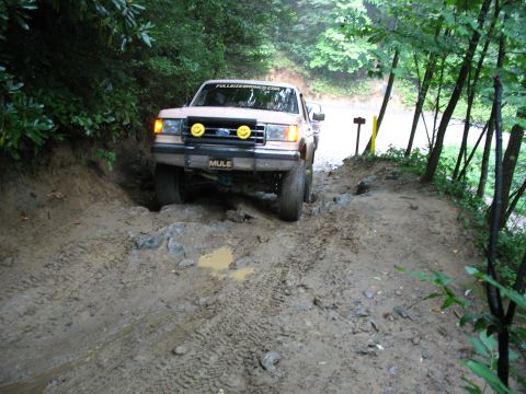 1995 Ford C-350 (Centurion Conversions) - Tan Ford F-Series truck with smiley face lights on bumper navigates a muddy, rocky trail.
