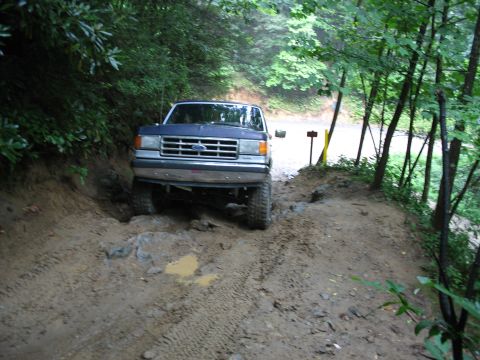 1995 Ford C-350 (Centurion Conversions) - A blue Ford F-Series truck struggles on a muddy, off-road trail surrounded by trees.