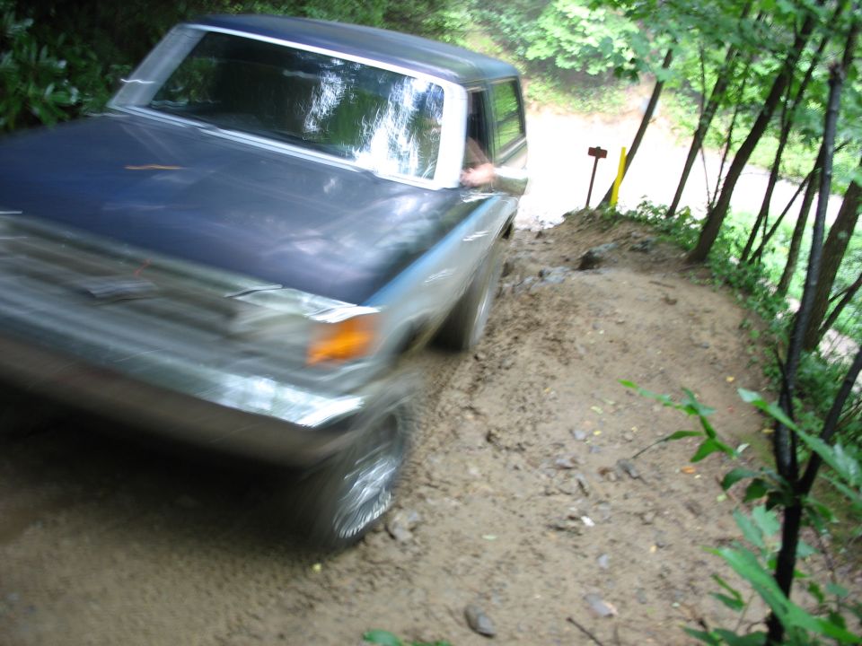 Old pickup truck driving on a muddy, wooded trail. Motion blur is present