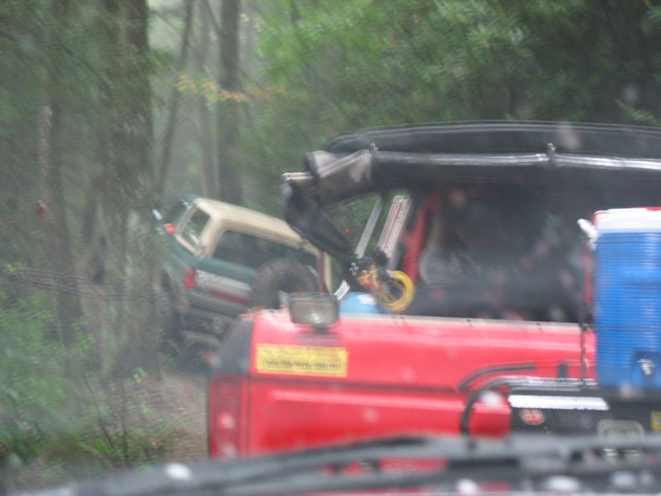 Two off-road vehicles are stuck in a wooded area, one is green and tan, the other is red