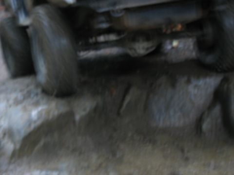 1995 Ford C-350 (Centurion Conversions) - The undercarriage and tires of a vehicle are visible, covered in mud, on an uneven terrain.