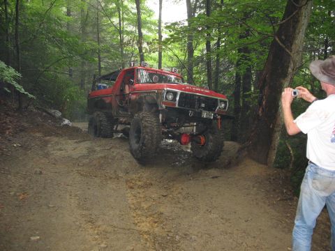1995 Ford C-350 (Centurion Conversions) - A man photographs a heavily modified red Ford Bronco navigating a muddy off-road trail.