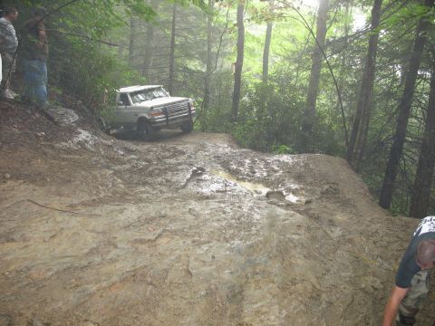 1995 Ford C-350 (Centurion Conversions) - A truck attempts to climb a difficult muddy incline in a wooded area.