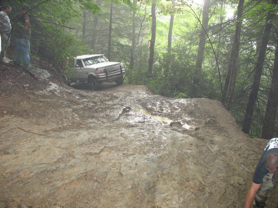 Silver pickup truck navigating a steep, muddy hill in a forest