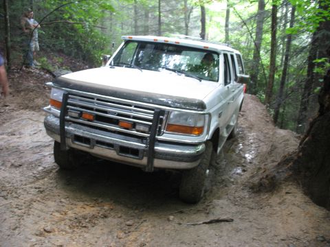 1995 Ford C-350 (Centurion Conversions) - A white Ford truck navigates a wet and muddy path through a dense forest.