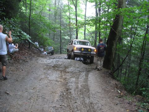 1995 Ford C-350 (Centurion Conversions) - A tan Ford Bronco navigates a difficult muddy trail while another vehicle is stuck in the ditch to the left.