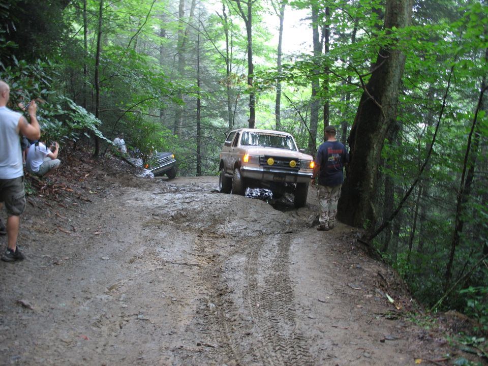 Tan Ford Bronco on muddy trail with another vehicle stuck in ditch