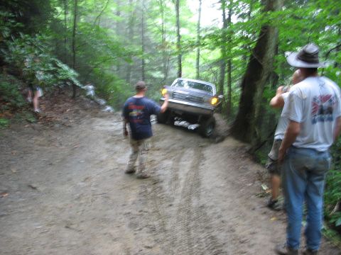 1995 Ford C-350 (Centurion Conversions) - A Ford F-Series truck navigates a challenging muddy path in a wooded area.