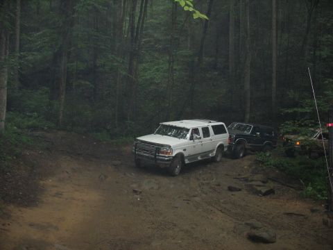1995 Ford C-350 (Centurion Conversions) - Three SUVs navigate a muddy, wooded trail during an off-road excursion.