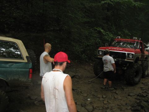1995 Ford C-350 (Centurion Conversions) - A red 1979 Ford F-Series truck with large tires is being winched on a muddy trail, with another vehicle partially visible.