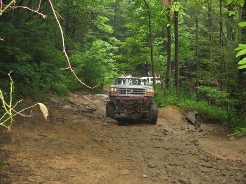 1995 Ford C-350 (Centurion Conversions) - A modified Ford truck navigates a challenging off-road trail through a dense forest.
