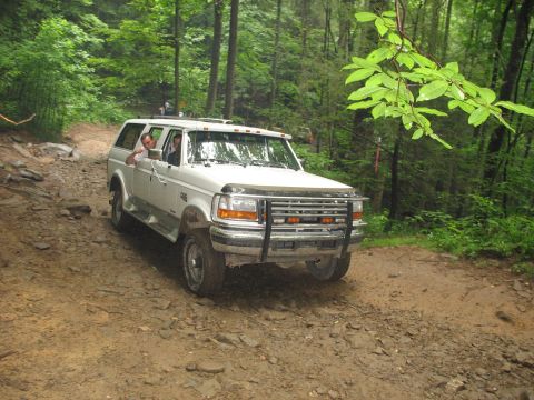 1995 Ford C-350 (Centurion Conversions) - A white Ford SUV navigates a muddy, wooded trail with another vehicle visible in the background.