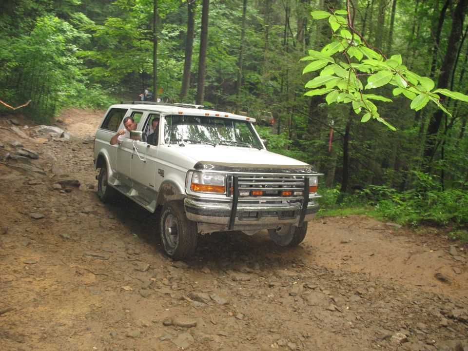 White Ford SUV with a brush guard on a dirt road in a forest