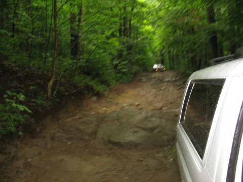 1995 Ford C-350 (Centurion Conversions) - Two vehicles navigate a challenging muddy trail through a dense forest.