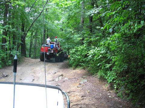 1995 Ford C-350 (Centurion Conversions) - Two vehicles navigate a rough, wooded trail, with one truck ahead on the path.