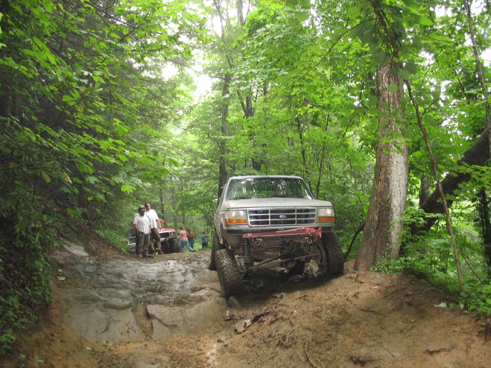Silver Ford F-Series truck with off-road modifications navigating a muddy trail