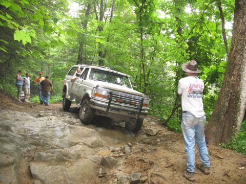 1995 Ford C-350 (Centurion Conversions) - A white Ford Bronco tackles a challenging rocky trail, demonstrating its off-road capabilities. The vehicle's body style suggests a 1992 mo…