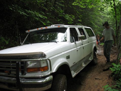 1995 Ford C-350 (Centurion Conversions) - White 1995 Ford C-350 (Centurion Conversions) navigates a rough, wooded trail.