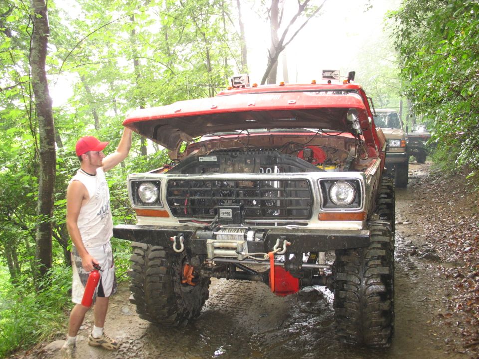 Red Ford truck with hood open, front view, large tires, winch, off-road modifications