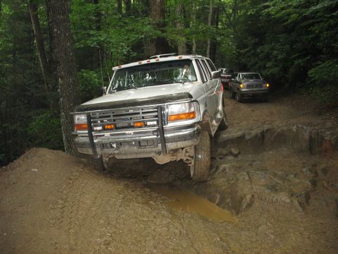 1995 Ford C-350 (Centurion Conversions) - A white 1995 Ford C-350 (Centurion Conversions) navigates a challenging muddy trail with another truck following behind.