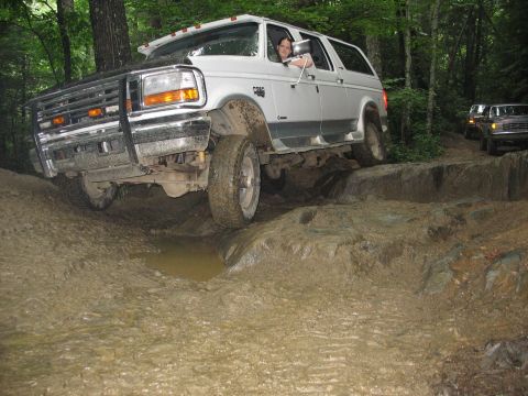 1995 Ford C-350 (Centurion Conversions) - A white Ford Bronco SUV tackles a challenging muddy and rocky off-road course.