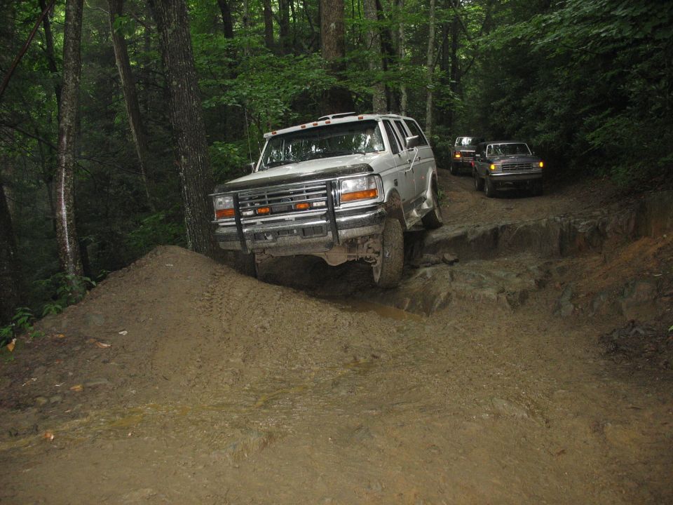 Silver SUV with a brush guard driving on a muddy, rocky trail in a forest