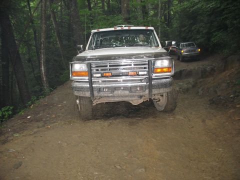 1995 Ford C-350 (Centurion Conversions) - A white Ford F-Series truck navigates a challenging, muddy off-road trail with another vehicle following.