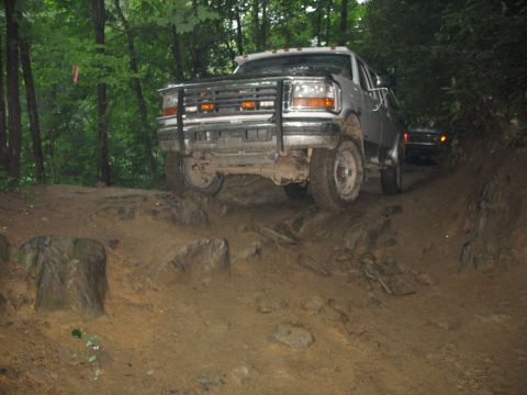 1995 Ford C-350 (Centurion Conversions) - A silver 1995 Ford C-350 (Centurion Conversions) navigates a challenging rocky and muddy trail with another vehicle visible behind it.