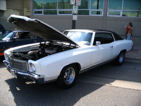 1993 Ford Taurus - White 1970s Chevrolet Monte Carlo coupe with black vinyl top and open hood at a car show.