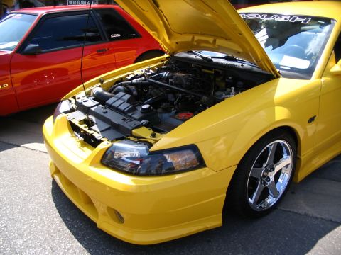 1993 Ford Taurus - Yellow 2000s Ford Mustang with hood open, parked next to a red Mustang at a car show.