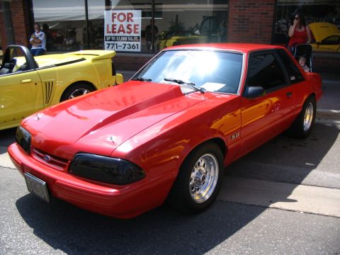 1993 Ford Taurus - A red 1993 Ford Mustang is parked on the street next to a yellow convertible, with a 'For Lease' sign in the background.