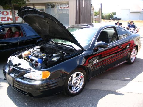 1993 Ford Taurus - Black Pontiac Grand Am coupe with hood open, parked next to another vehicle at an outdoor event.