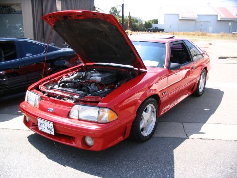 1993 Ford Taurus - A red 1993 Ford Mustang GT is parked outside with its hood open, revealing the engine bay.
